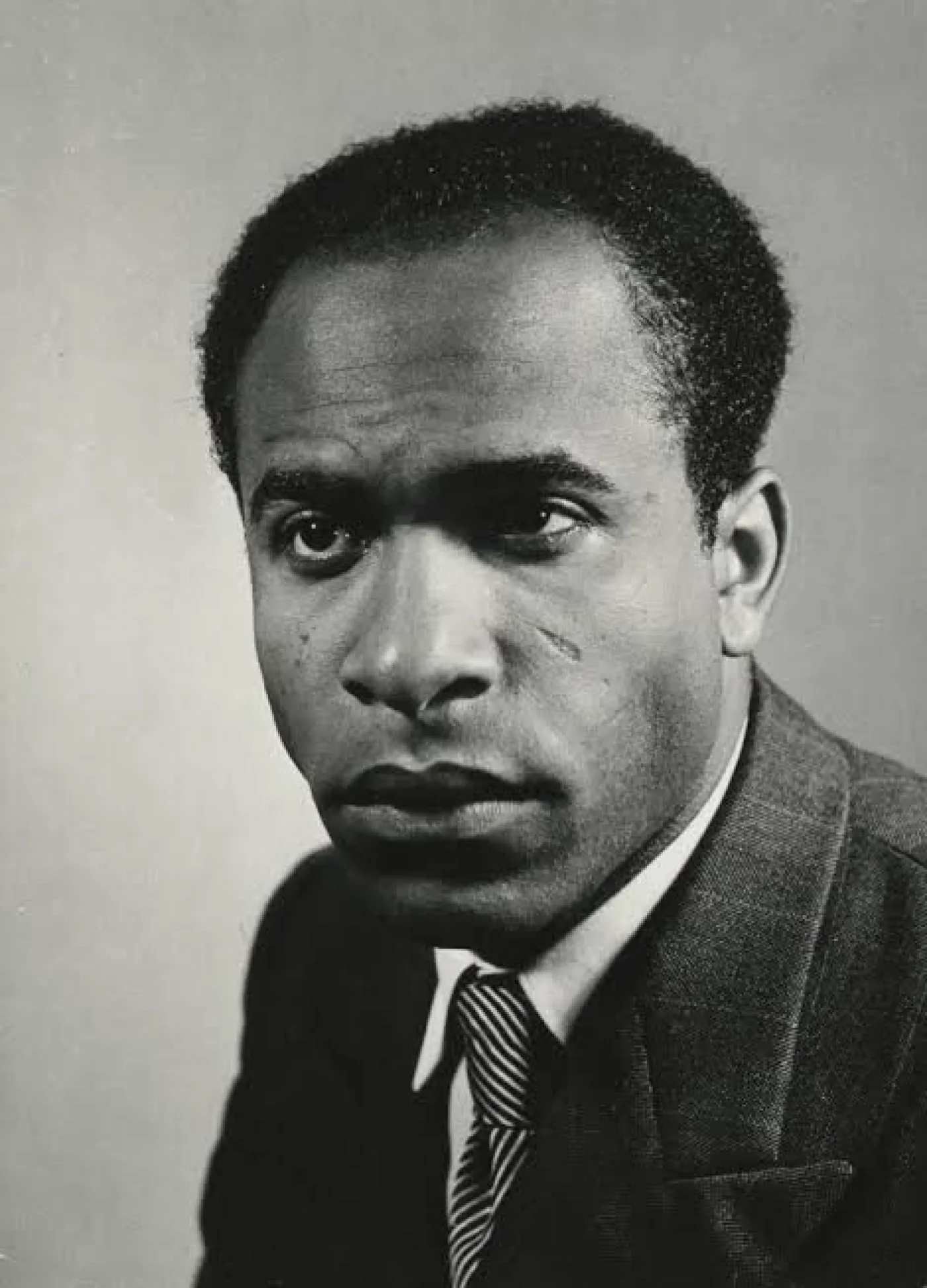 Black-and-white portrait photograph of Frantz Fanon: a young man in a suit with a serious gaze