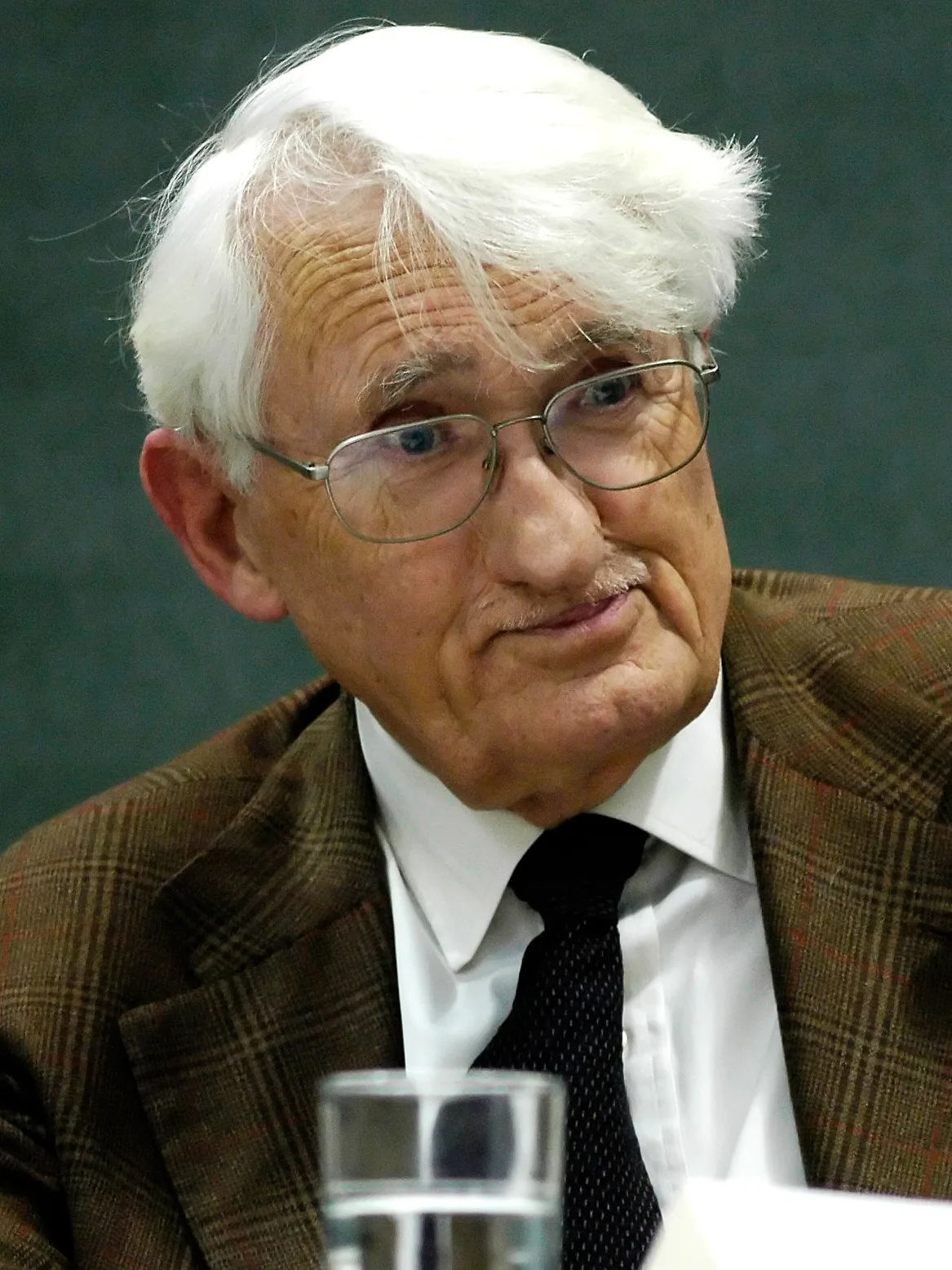 An older man with white hair, fine-rimmed glasses, and tightly closed lips listening intently — a close-up portrait of Jürgen Habermas taken in Munich in 2008